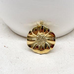Könnte beinhalten: Ein goldfarbener Blumenanhänger mit einer strukturierten Oberfläche. Die Blume hat fünf Blütenblätter und eine Mitte mit einem erhabenen, strukturierten Design.