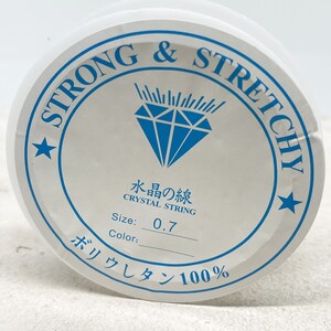 Puede incluir: Una bobina blanca de hilo de cristal fuerte y el&aacute;stico, etiquetada como "Strong & Stretchy" y "Crystal String". La bobina tiene un tama&ntilde;o de 0,7 mm y est&aacute; hecha de 100% poliuretano.
