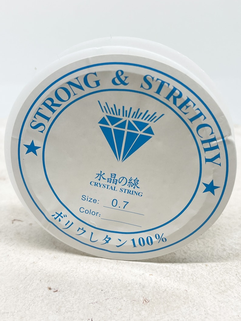 Puede incluir: Una bobina blanca de hilo de cristal fuerte y el&aacute;stico, etiquetada como "Strong & Stretchy" y "Crystal String". La bobina tiene un tama&ntilde;o de 0,7 mm y est&aacute; hecha de 100% poliuretano.