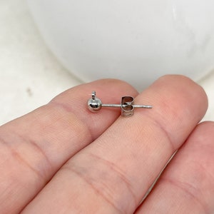 May include: A silver earring with a small ball at the end and a post with a butterfly back.