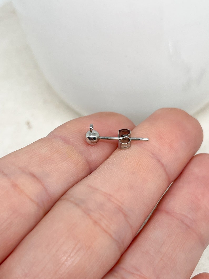 May include: A silver earring with a small ball at the end and a post with a butterfly back.