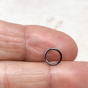 May include: A small, silver jump ring. The ring is about 1/2 inch in diameter and is made of metal.