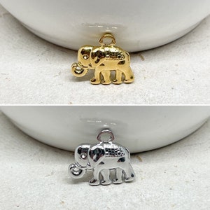 Könnte beinhalten: Zwei Elefanten-Anhänger, einer golden und einer silbern, mit einer Öse oben zum Anbringen an eine Halskette oder ein Armband.