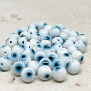 Könnte beinhalten: Ein Haufen weißer runder Perlen mit blauen und schwarzen Augenmustern.