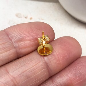 May include: Gold-toned earring finding with a round base and a post for attaching an earring.