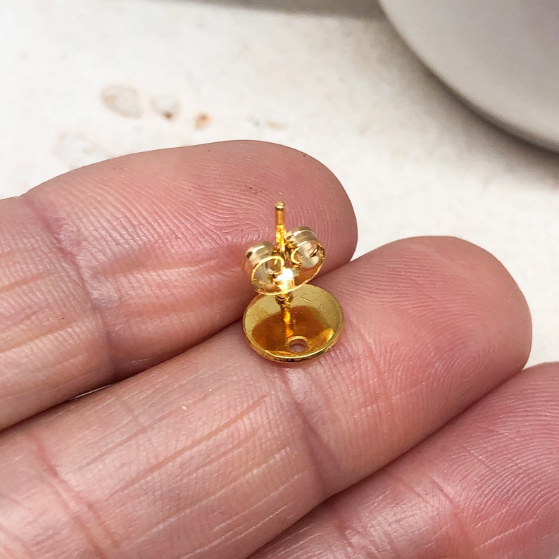 May include: Gold-toned earring finding with a round base and a post for attaching an earring.