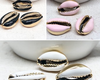 May include: Three pairs of cowrie shell charms with gold trim. The shells are black, pink, and white.