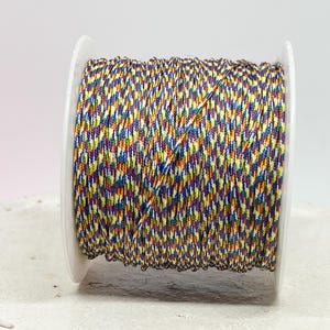 Könnte beinhalten: Eine Spule mit mehrfarbigem Kordel, eng auf einer weißen Kunststoffspule aufgewickelt. Das Kordel weist ein lebendiges Muster aus gelben, blauen, roten und violetten Fäden auf, wodurch ein strukturiertes Aussehen entsteht. Ideal für Bastel- und DIY-Projekte.