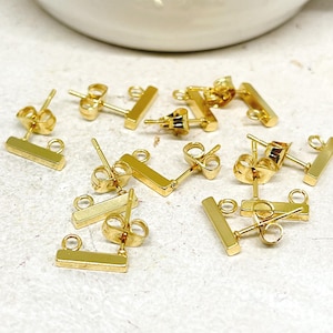 Op de afbeelding: Een verzameling goudkleurige oorbelstud-bevindingen. De oorbellen hebben een rechthoekige staafvorm met een lus om bedels aan te bevestigen. De oorbelpalen en -sluitingen zijn ook goudkleurig.