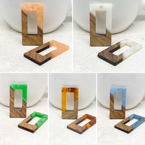 Könnte beinhalten: Sechs rechteckige Holz-Anhänger-Rohlinge mit einem Loch oben. Jeder Rohling besteht aus Holz mit einem Halbkreis aus Harz auf der oberen Hälfte. Die Harzfarben sind orange, weiß, grün, bernstein, blau und hellgrün.