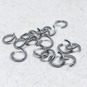 May include: A pile of silver jump rings, a type of jewelry finding used for connecting chains, cords, and other jewelry components.