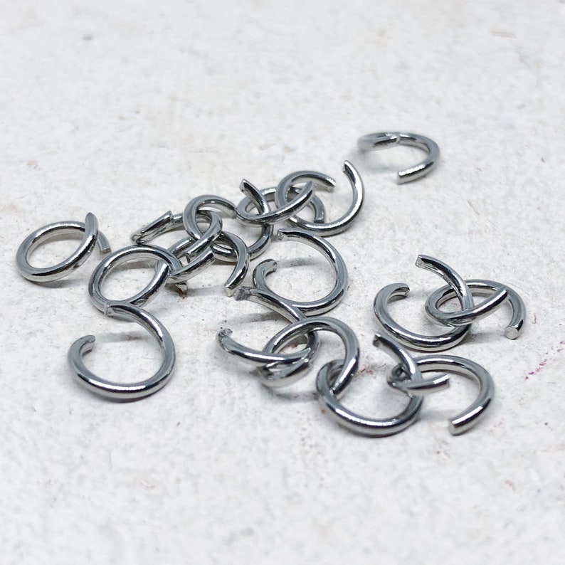 May include: A pile of silver jump rings, a type of jewelry finding used for connecting chains, cords, and other jewelry components.