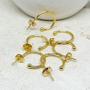May include: Four gold hoop earrings with a small ball at the end of each hoop. The earrings are on a white surface.