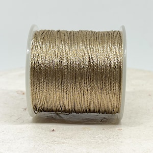 May include: A spool of gold metallic thread. The thread is wound tightly around a clear plastic spool.