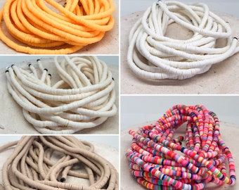 Könnte beinhalten: Sortiment an bunten Keramikperlen in verschiedenen Farben, darunter Weiß, Beige, Orange und Mehrfarbig. Die Perlen sind in Stapeln auf einer weißen Oberfläche angeordnet.