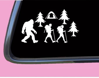 May include: White vinyl decal of a Bigfoot, two hikers, a tent, and trees. The decal is on a black background.