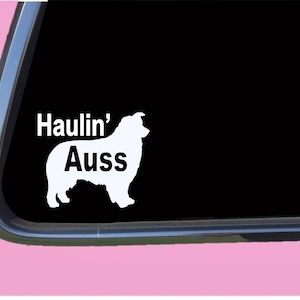 May include: White vinyl decal of an Australian Shepherd silhouette with the text "Haulin' Auss" on a black car window.