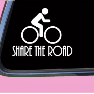 Peut inclure: Autocollant en vinyle blanc avec une silhouette d'une personne à vélo et le texte "SHARE THE ROAD".