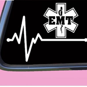 May include: White EMT sticker featuring a heartbeat line on a black background. The EMT logo is a white star of life with the letters "EMT" in bold, black font. The sticker is displayed on a car window.
