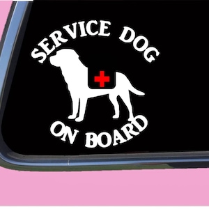 May include: White vinyl sticker with a black background. The sticker features a white silhouette of a dog with a red cross on its back. The text "SERVICE DOG ON BOARD" is in a white circle around the dog.