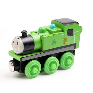 May include: A green wooden toy train engine with a black face and wheels. The engine has the number "11" and the letters "GWR" on the side.