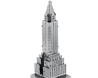 Puede incluir: Modelo metálico plateado del edificio Chrysler. El modelo es una réplica detallada del icónico rascacielos, con intrincados detalles arquitectónicos. El edificio tiene un diseño escalonado con una aguja en la parte superior y una base rectangular.