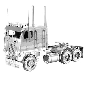 Op de afbeelding: Een zilverkleurig metalen model van een vrachtwagen. Het model heeft een gedetailleerde constructie, inclusief de cabine, de trailerkoppeling en meerdere wielen. Het model heeft een gedetailleerde grille, koplampen en uitlaatpijpen. Het model is een verzamelobject.