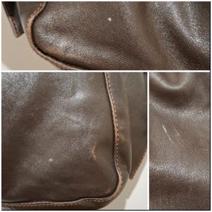 May include: Close-up of a brown leather bag, showing the texture and stitching details. The leather has some wear and tear, with visible scratches and marks. The bag's edges are reinforced with stitching.