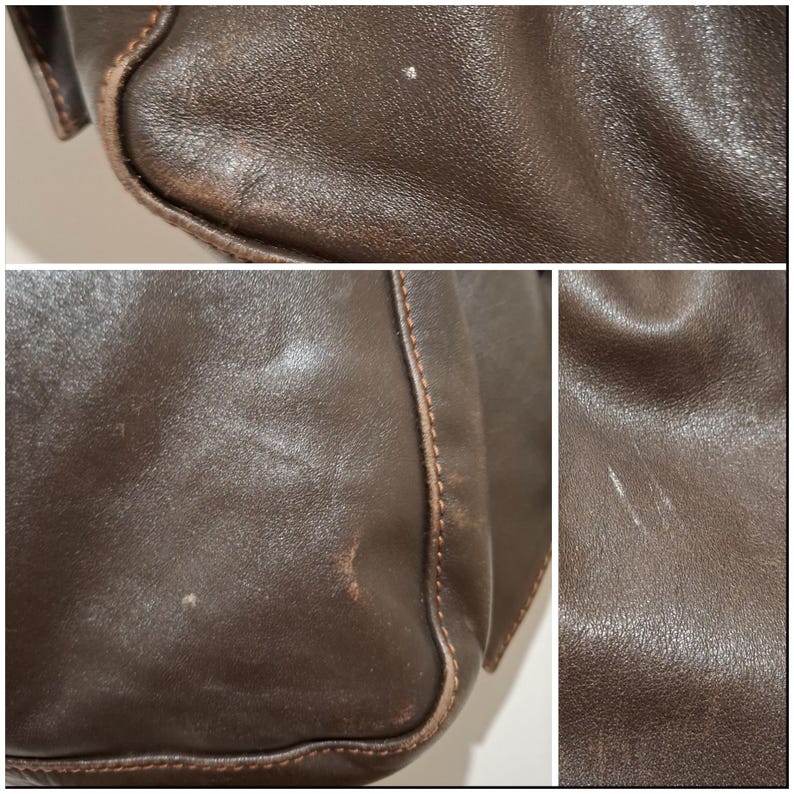 May include: Close-up of a brown leather bag, showing the texture and stitching details. The leather has some wear and tear, with visible scratches and marks. The bag's edges are reinforced with stitching.