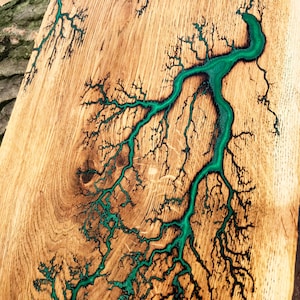 May include: A wooden board with a natural wood grain finish. The board has a green epoxy resin filling in the cracks and knots, creating a unique and decorative piece.