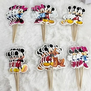May include: A selection of Mickey Mouse and Minnie Mouse cupcake toppers. Each topper displays a cartoon image of the characters in different poses, with a wooden stick attached for easy insertion into cupcakes. The toppers are colourful and suitable for a themed party.