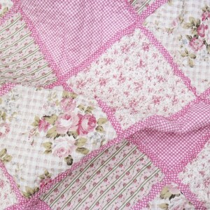 Könnte beinhalten: Ein Patchwork-Quilt mit Blumen- und Vichy-Mustern in Rosa, Weiß und Grün. Der Quilt besteht aus Quadraten, die mit rosa Bordüren zusammengenäht sind und ein dekoratives Textil bilden.