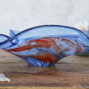 May include: A decorative glass bowl with a wavy rim. The bowl is a vibrant blue with red and white swirls throughout. The bowl sits on a wooden surface.