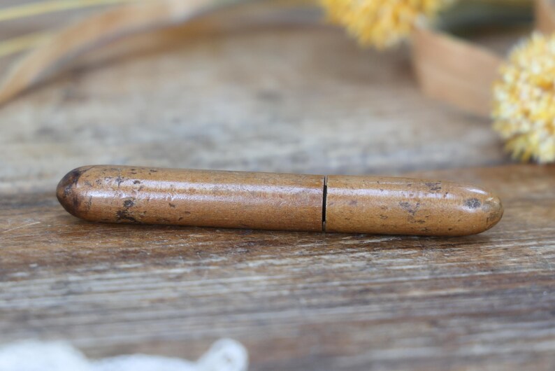 May include: A vintage, cylindrical wooden container with a light brown finish and a split in the middle. The container has rounded ends and a slightly textured surface, resting on a wooden surface.