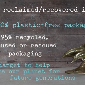 May include: A bronze dolphin sculpture with two dolphins leaping from the water. The background is a rustic wooden surface with text that reads "100% reclaimed/recovered items" and "100% plastic-free packaging."