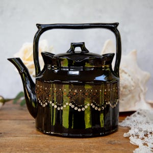 May include: A black teapot with gold and white accents. The teapot has a decorative design around the middle and a shiny black finish.