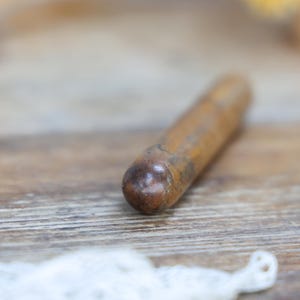 May include: A wooden object with a rounded end, likely a tool or component, lies on a wooden surface. The object is cylindrical and appears to be made of a light brown wood. The background is blurred, suggesting a shallow depth of field.