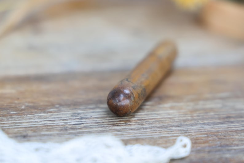 May include: A wooden object with a rounded end, likely a tool or component, lies on a wooden surface. The object is cylindrical and appears to be made of a light brown wood. The background is blurred, suggesting a shallow depth of field.