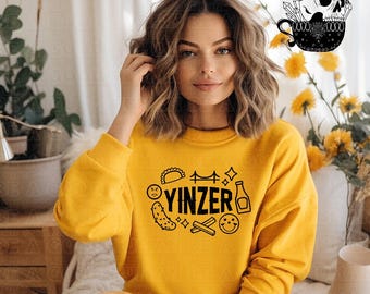 May include: A yellow sweatshirt with a black graphic design that says "YINZER" and includes images of a pickle, a pretzel, a bridge, and a bottle of ketchup.