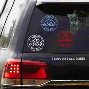 May include: Four different color variations of a round sticker with the text "Support Wildlife Raise Boys" and a mountain range graphic. The sticker is on the back window of a black SUV.
