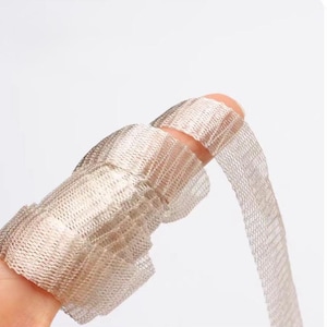 May include: A finger wrapped in a beige mesh material is shown in close-up. The mesh is tightly woven, creating a textured appearance. The material is partially wrapped around the finger, with a loose end extending outwards. The background is a soft, neutral colour.