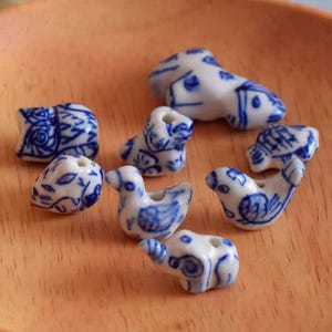 May include: A collection of blue and white porcelain beads featuring various animal designs, including birds, an elephant, and an owl. The beads are hand-painted with intricate details and are perfect for jewellery making or crafting.