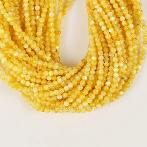 May include: A strand of yellow round beads with a pearlescent finish. The beads are strung together on a clear thread.