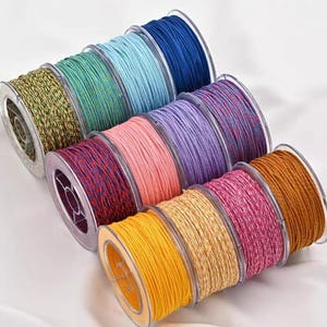 Puede incluir: Una colección de coloridas bobinas de cordón en varios tonos, incluyendo azul, verde, rosa y amarillo. Los cordones están enrollados firmemente en bobinas de plástico transparente, mostrando su textura y variaciones de color. Ideal para manualidades y bisutería.