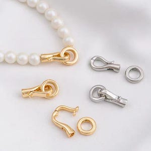 Puede incluir: Un juego de cierres dorados y plateados para la elaboración de joyas. Los cierres son de varios estilos, incluyendo un cierre de langosta, un cierre de palanca y un cierre de anillo.