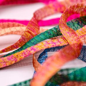 以下が含まれることがあります： メタリックなオープンウィーブメッシュの質感が特徴の、細く柔軟なリボンのコレクション。ホットピンク、エメラルドグリーン、ブライトオレンジ、ディープブルーなどの鮮やかなグラデーションカラーのリボンが、緩やかに絡み合って配置されています。
