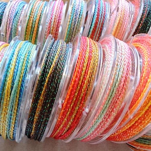 May include: Spools of colorful braided cord in various hues, including blue, yellow, green, orange, and pink. The cords are wound on clear plastic spools, creating a vibrant display. Ideal for crafting and jewelry making.