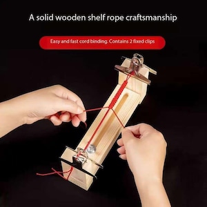 May include: A wooden tool for making cord bracelets. The tool has two clamps and a groove for the cord to run through. The cord is red and is being tied by hand.