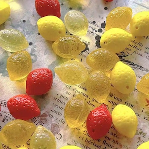 May include: An overhead shot displays a collection of colorful, candy-like fruit shapes. The assortment includes translucent yellow lemon shapes and vibrant red strawberry shapes, scattered across a patterned surface.