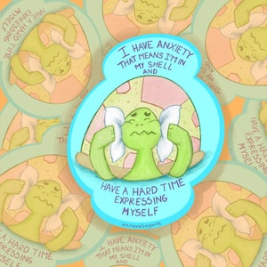 May include: A green turtle with white eyes and a pink shell is holding two white pillows to its ears. The turtle is surrounded by a blue circle with the text "I have anxiety that means I'm in my shell and have a hard time expressing myself." The text is in black and white. The background is a light blue color.